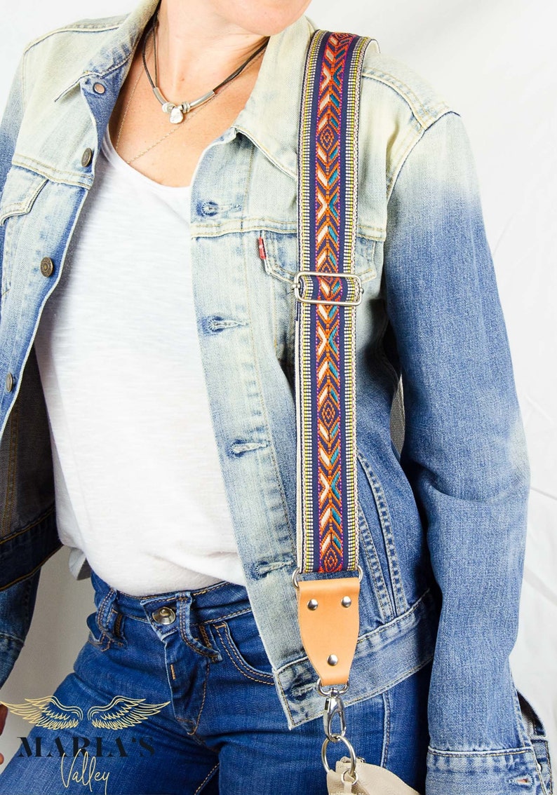 Pode incluir: Um close-up de uma mulher vestindo uma jaqueta de jeans e jeans azul. Ela est&aacute; usando uma al&ccedil;a estampada colorida para uma bolsa sobre o ombro. A al&ccedil;a tem um detalhe de couro e um fecho de metal prateado.