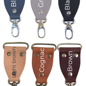 May include: Six leather keychains with different colors and finishes. The colors are blue, gray, black, light brown, cognac, and brown. Each keychain has a silver or brass swivel hook.