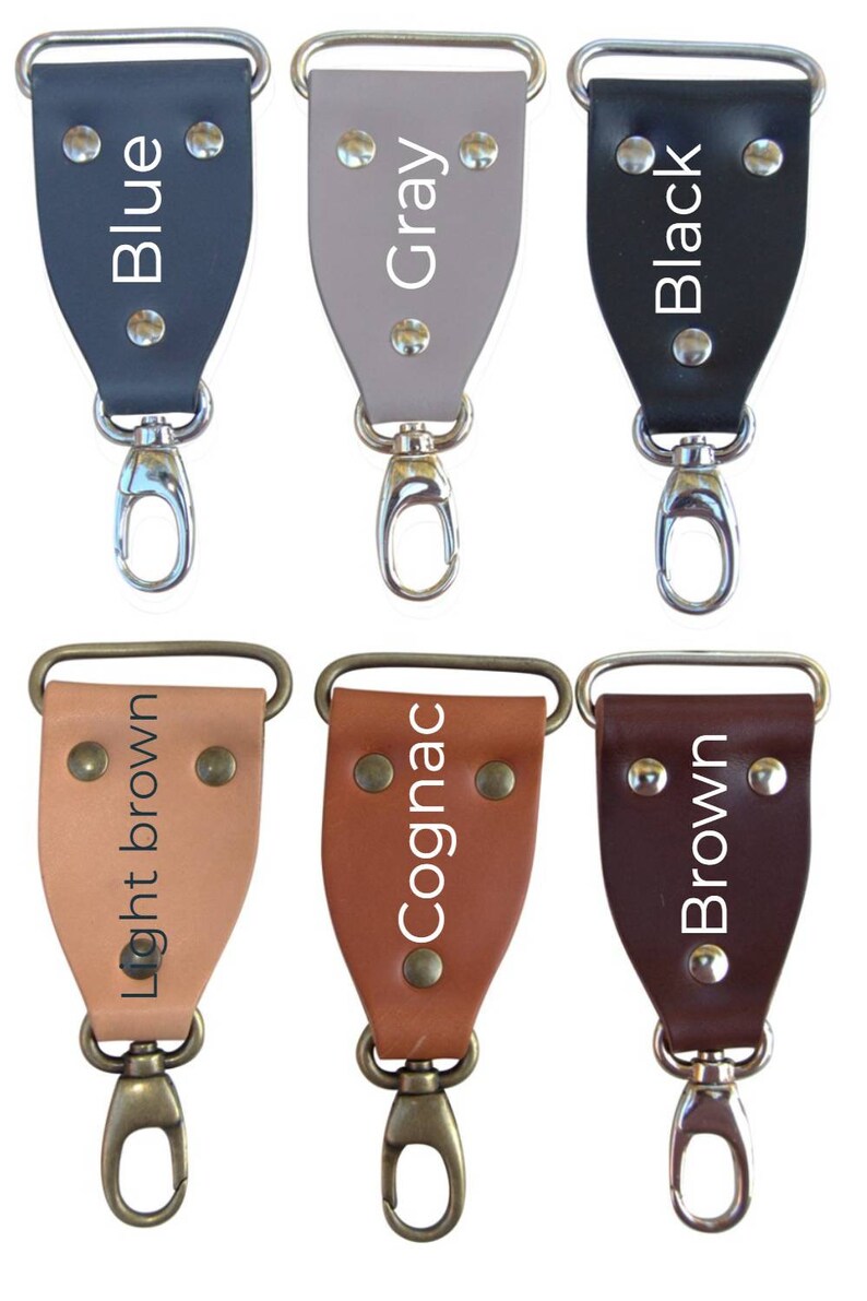 May include: Six leather keychains with different colors and finishes. The colors are blue, gray, black, light brown, cognac, and brown. Each keychain has a silver or brass swivel hook.