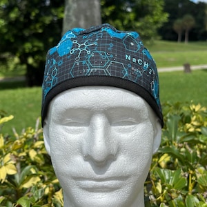 May include: A black and blue surgical scrub cap with a molecular structure pattern and the text "NaCH". The cap has a black band around the bottom. The cap is displayed on a white mannequin head.