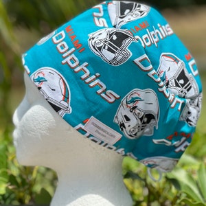 May include: Turquoise blue surgical scrub cap with a white and orange Miami Dolphins pattern. The cap has a white label that says "GSSurgicalCaps Etsy.com".