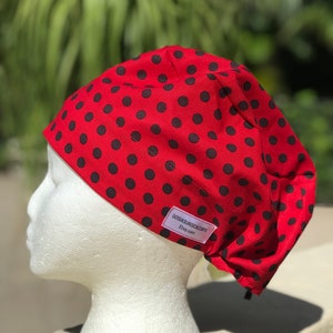 May include: Red surgical scrub cap with black polka dots. The cap has a label that reads "Gossasurgicalcaps Etsy.com".