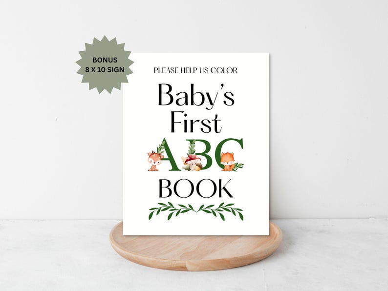 Puede incluir: Un letrero blanco con el texto "Baby's First ABC Book" en negro y verde. El letrero incluye ilustraciones de animales del bosque y vegetaci&oacute;n. Se incluye un letrero adicional de 20,3 x 25,4 cm.