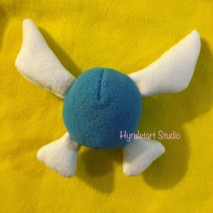 May include: A blue and white plush toy with wings. The toy is shaped like a round ball with two wings extending out from the sides. The wings are white and the ball is blue.