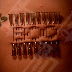 May include: A close-up of a person's skin with multiple small, clear, plastic tubes attached to it. The tubes are arranged in two rows, with the needles pointing towards the viewer. The tubes are attached to the skin with small metal pins.