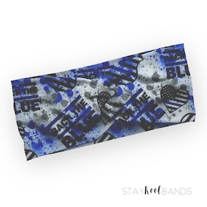 May include: A blue and white headband with a splatter paint design and the text "Back the Blue" repeated throughout. The headband also features a heart with a thin blue line.