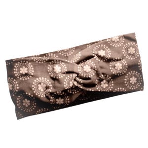 May include: A brown headband with a white floral pattern. The headband is twisted and knotted.