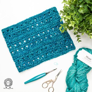 May include: A woman wearing a teal blue crocheted infinity scarf and a black top. She is smiling and wearing glasses.