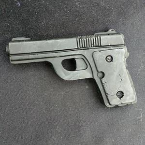 Może przedstawiać: Mały, czarny pistolet zabawkowy z teksturowanym uchwytem i zamkiem. Zabawkowy pistolet ma spust, zatrzask magazynka i celownik. Pistolet jest wykonany z tworzywa sztucznego i wydaje się być repliką prawdziwej broni palnej.