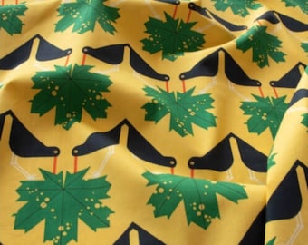 May include: Yellow fabric with a repeating pattern of black birds and green leaves. The birds have long, thin legs and are facing to the right. The leaves are a dark green with a light green center and have a speckled pattern.