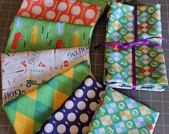 Peut inclure: Une collection de carrés de tissu pliés présentant des motifs sur le thème du golf, notamment des balles, des clubs, des sacs, des chariots et des imprimés argyle dans des tons vert, orange, blanc, jaune et bleu marine, avec un lot noué d'un ruban violet.