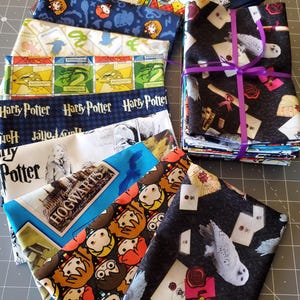 Op de afbeelding: Een verzameling kleurrijke Harry Potter-stoffenbundels. De stoffen hebben verschillende ontwerpen, waaronder Zweinstein, uilen en karakterillustraties. Sommige bundels zijn vastgebonden met een paars lint.