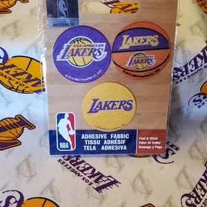 Könnte beinhalten: Vier runde, selbstklebende Stoff-Patches mit dem Logo der Los Angeles Lakers. Die Patches sind gelb, lila und orange mit einer Basketball-Grafik. Der Text "Los Angeles Lakers" und "NBA" ist auf den Patches sichtbar.