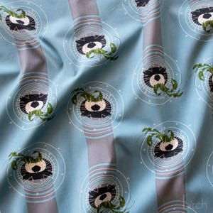 May include: Light blue fabric with a repeating pattern of black and white circular designs with green accents. Vertical gray stripes with light blue and white stripes run through the design. The fabric has a soft, flowing appearance.