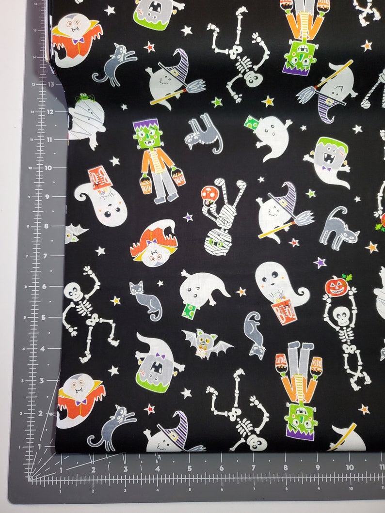 K&ouml;nnte beinhalten: Schwarzer Stoff mit einem Halloween-Motiv mit Geistern, Skeletten, Mumien, Flederm&auml;usen, Katzen und Sternen. Der Druck ist in verschiedenen Farben, darunter Orange, Gr&uuml;n, Wei&szlig; und Lila.