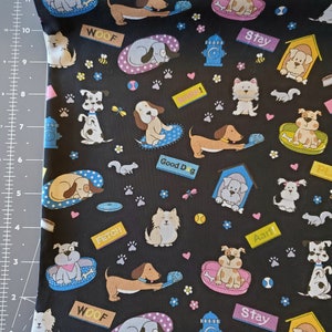 May include: Black fabric with a repeating pattern of dogs in various poses. The dogs are wearing collars and some have bones or toys. The fabric has the words "Woof", "Fetch", "Stay", "Good Dog", and "Aarf!" printed on it.