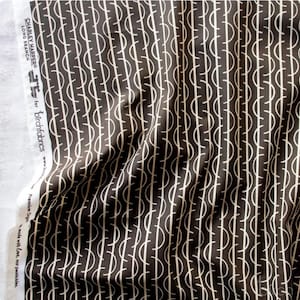 May include: A dark brown fabric featuring a repeating pattern of thin white vertical lines intersected by white semi-circles. The white selvage edge displays the text: CHARLEY HARPER LONG BRANCH for birchfabrics Premium Organic.