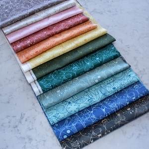 May include: A stack of 10 different fabric swatches with geometric patterns in shades of gray, pink, orange, yellow, green, blue, and black. The fabric swatches are arranged in a rainbow pattern from lightest to darkest.