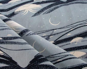 May include: Light blue fabric with a repeating pattern of white jellyfish-like shapes, black brushstrokes, crescent moons, and small white dots. The fabric is folded, showing the texture and design. The overall theme is a celestial or marine design.