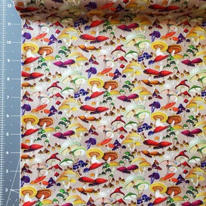 Pode incluir: Um rolo de tecido com um padr&atilde;o de cogumelos colorido. O design inclui v&aacute;rios tipos de cogumelos em tons de vermelho, amarelo, roxo e verde, sobre um fundo neutro. O tecido &eacute; provavelmente algod&atilde;o ou similar.