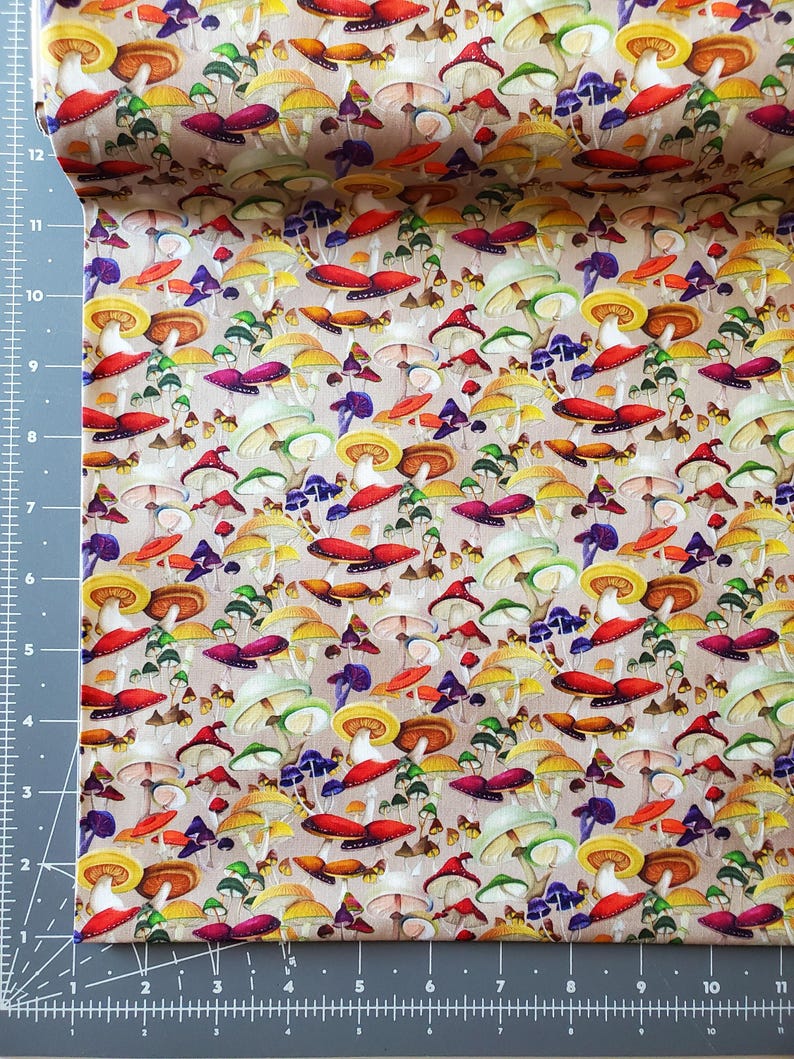 Pode incluir: Um rolo de tecido com um padr&atilde;o de cogumelos colorido. O design inclui v&aacute;rios tipos de cogumelos em tons de vermelho, amarelo, roxo e verde, sobre um fundo neutro. O tecido &eacute; provavelmente algod&atilde;o ou similar.