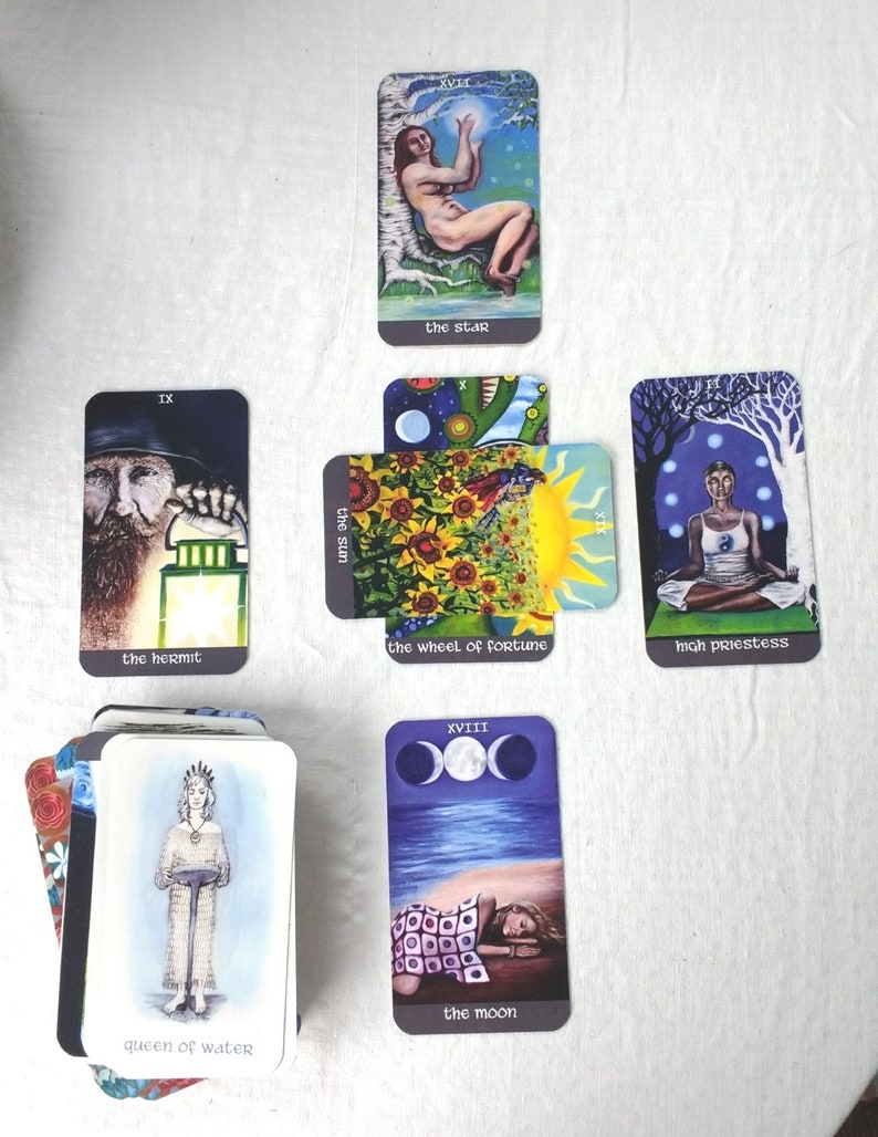 May include: A selection of tarot cards with diverse illustrations. Cards include "The Star," "The Hermit," "The Wheel of Fortune," "High Priestess," "The Moon," and "Queen of Water." The cards are laid out on a white cloth.