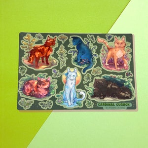 Op de afbeelding: Een stickervel met illustraties van zes katten in verschillende kleuren en poses, omringd door bloemmotieven. De katten zijn afgebeeld in tinten rood, blauw, oranje en zwart, met een lichtblauwe kat in het midden. De tekst "CARDINAL CUSACK" staat onderaan.