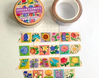 以下が含まれることがあります： 「Garden Flowers」のマスキングテープのロールと、部分的にほどかれたテープ。テープには、さまざまな花のカラフルなイラストが明るい背景に描かれています。「Garden Flowers washi tape」の文字と、Instagramのハンドルネーム@cardinalcrownsが表示されています。