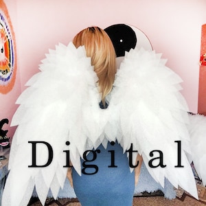 May include: White angel wings made of layered fabric. The wings are large and fluffy, with a layered design. The word "Digital" is printed in black on the wings. The person is wearing a blue dress.