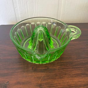 Peut inclure: Un presse-agrumes vintage en verre vert vif. Le presse-agrumes a un bol nervuré avec un bec verseur et une poignée. Le centre a un alésoir conique pour extraire le jus. Le presse-agrumes est en verre vert translucide.