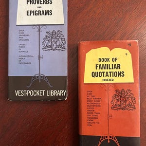 Könnte beinhalten: Zwei Vintage-Bücher der Vest-Pocket Library. Eines ist hellblau mit "Proverbs and Epigrams" auf dem Cover. Das andere ist rot mit "Book of Familiar Quotations" auf dem Cover. Beide Bücher haben einen schwarzen Sockel und ein dekoratives Emblem.