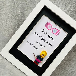 May include: A framed print featuring a quote from Luna Lovegood from the Harry Potter series. The quote reads "Don't worry, you're just as sane as I am." The print includes a Lego minifigure of Luna Lovegood wearing a lion hat and holding a wand.