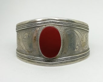 May include: A silver bracelet with an ornate design and a red stone in the center.