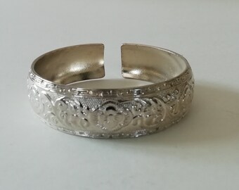 May include: A silver bangle bracelet with an intricate floral design.