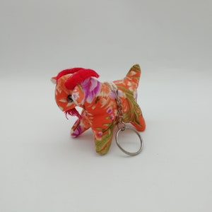 May include: A small orange and floral patterned goat keychain with red horns and a silver key ring.