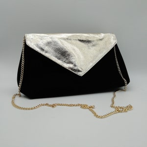 Op de afbeelding: Een zwarte clutch van fluweel met een gouden metalen klep en een gouden kettingband.