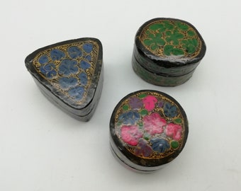 Könnte beinhalten: Drei kleine dekorative Schachteln mit aufwendigen Blumendesigns. Die Schachteln sind aus schwarzem Papiermaché gefertigt und mit goldenen, blauen, grünen, rosa und violetten Blumen bemalt.