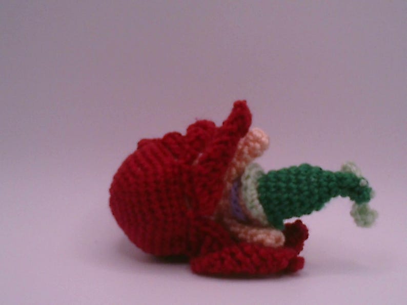 May include: A handmade, crocheted sculpture with a striking red base and a ruffled edge. It features green, cream, and pastel-coloured elements, set against a soft, neutral background. The piece displays a unique, textured aesthetic, showcasing the craft's detail.