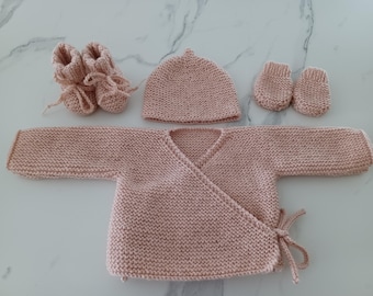 May include: A pink knitted baby outfit set including a hat, a cardigan, mittens, and booties.