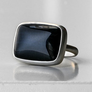 May include: A silver ring with a black rectangular gemstone. The ring has a smooth, polished finish.