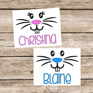 May include: Two white bunny face stickers with black outlines and pink and blue noses. The stickers have the names Christina and Blaine written below the faces.