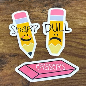 May include: Three colorful stickers: two pencils and an eraser. One pencil says "Sharp" with a smiling face, the other says "Dull" with a sad face. The eraser is pink with the word "Erasers".