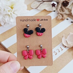 Può includere: Un paio di orecchini fatti a mano con un fiocco rosso e un design a testa di Topolino nero. Gli orecchini sono esposti su una carta marrone con il testo "Handmade with love".