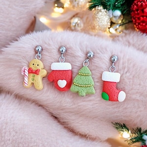 Può includere: Quattro paia di orecchini a tema natalizio con perni d'argento. Gli orecchini presentano un omino di pan di zenzero, un guanto, un albero di Natale e una calza.