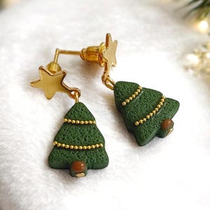 Pode incluir: Um par de brincos de árvore de Natal dourados com detalhes verdes e dourados. Cada brinco tem um pequeno charme de estrela dourada.