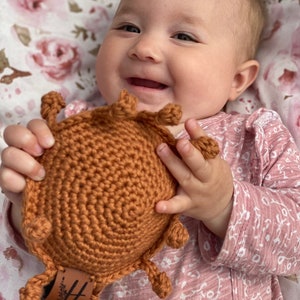 May include: A baby is holding a crocheted brown turtle toy with a leather tag that says "Handmade".