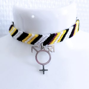 Op de afbeelding: Een vriendschapsarmband met gele, witte, zwarte en paarse strepen. De armband heeft een zilveren bedel met een transgender symbool.