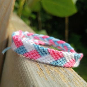 May include: A pink, blue, and white friendship bracelet with a chevron pattern.