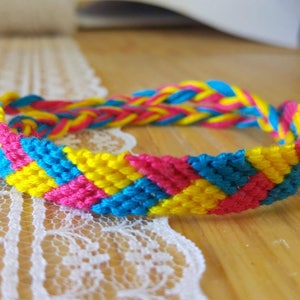 Op de afbeelding: Een vriendschapsarmband geweven met gele, blauwe en roze draden in een chevron-patroon.