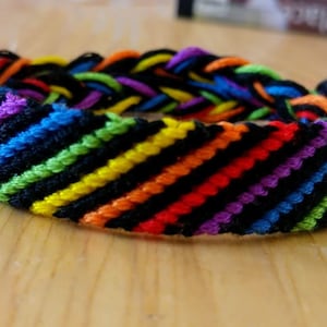 Pulseira da amizade multicolorida em preto e arco-íris, orgulho LGBTQ+, queer.